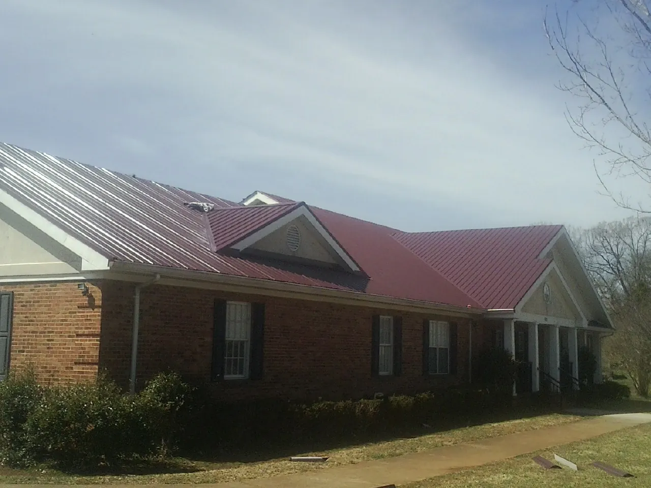 Red metal roof with gabled entries on a long brick building, from a Hail Damage Roof Repair job in Auburn