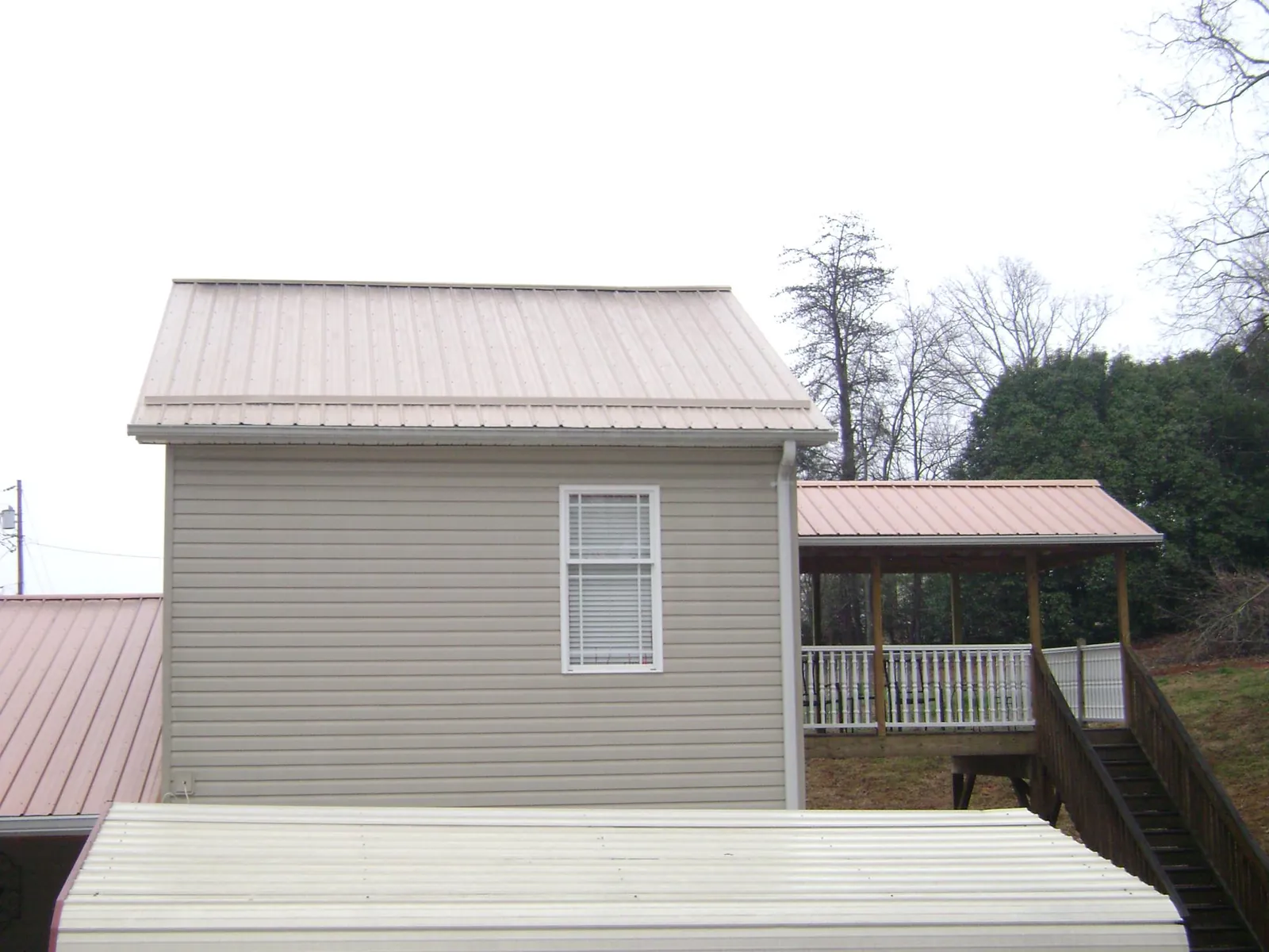 Tan metal roofs on a two story addition and attached porch, from a Roof Replacement job in Auburn